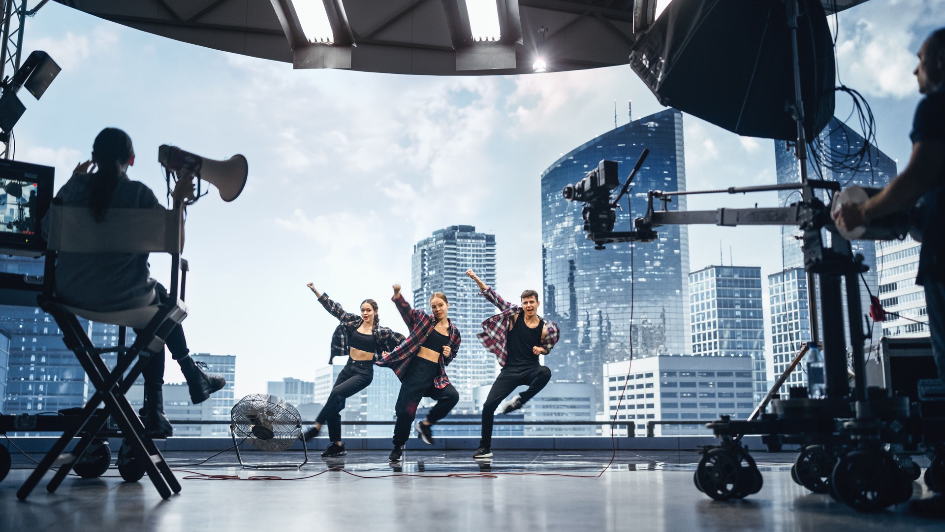 Music Clip Studio Set: Shooting Hip Hop Video Dance Scene with Three Professionals Dancers Performing on Stage with Big Led Screen with Modern City Background. Director and Cameraman in Backstage.